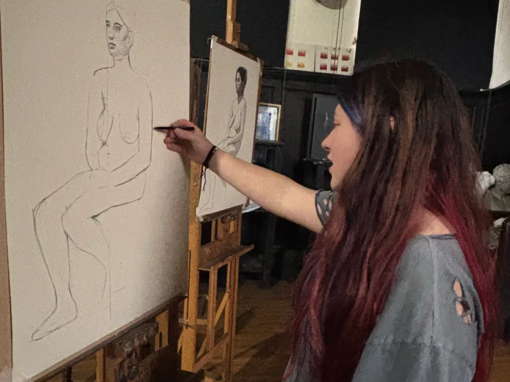 A student refining a life drawing on a large canvas using the sight-size method, focusing on proportion and tonal accuracy in a professional studio environment.