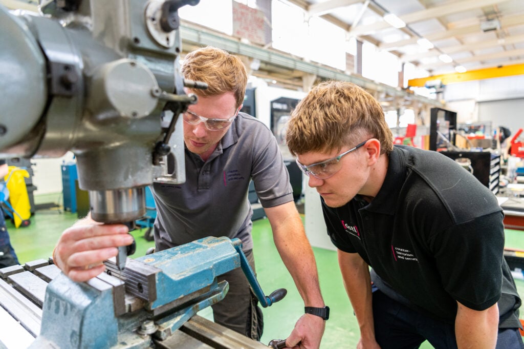 Apprentice working on some equipment with an employer observing and guiding him.