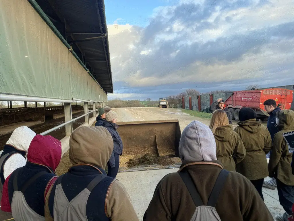 Agriculture students stand with a farm consultant beside farm equipment during a practical learning visit linked to their course.