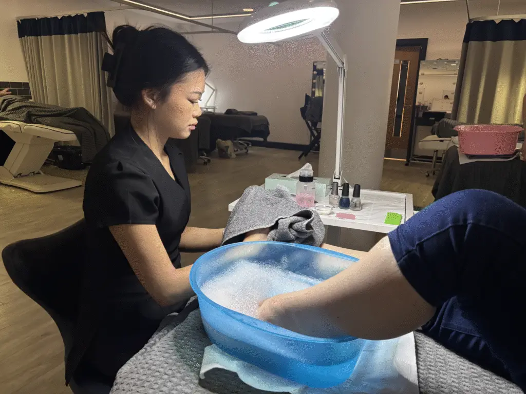 Client soaking feed in bowl of water while student prepares tools for a pedicure