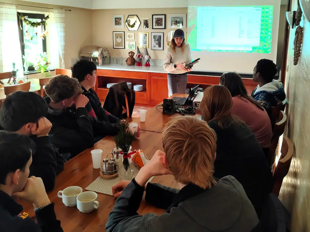 Female teacher leading a classroom of students, sat round a table.