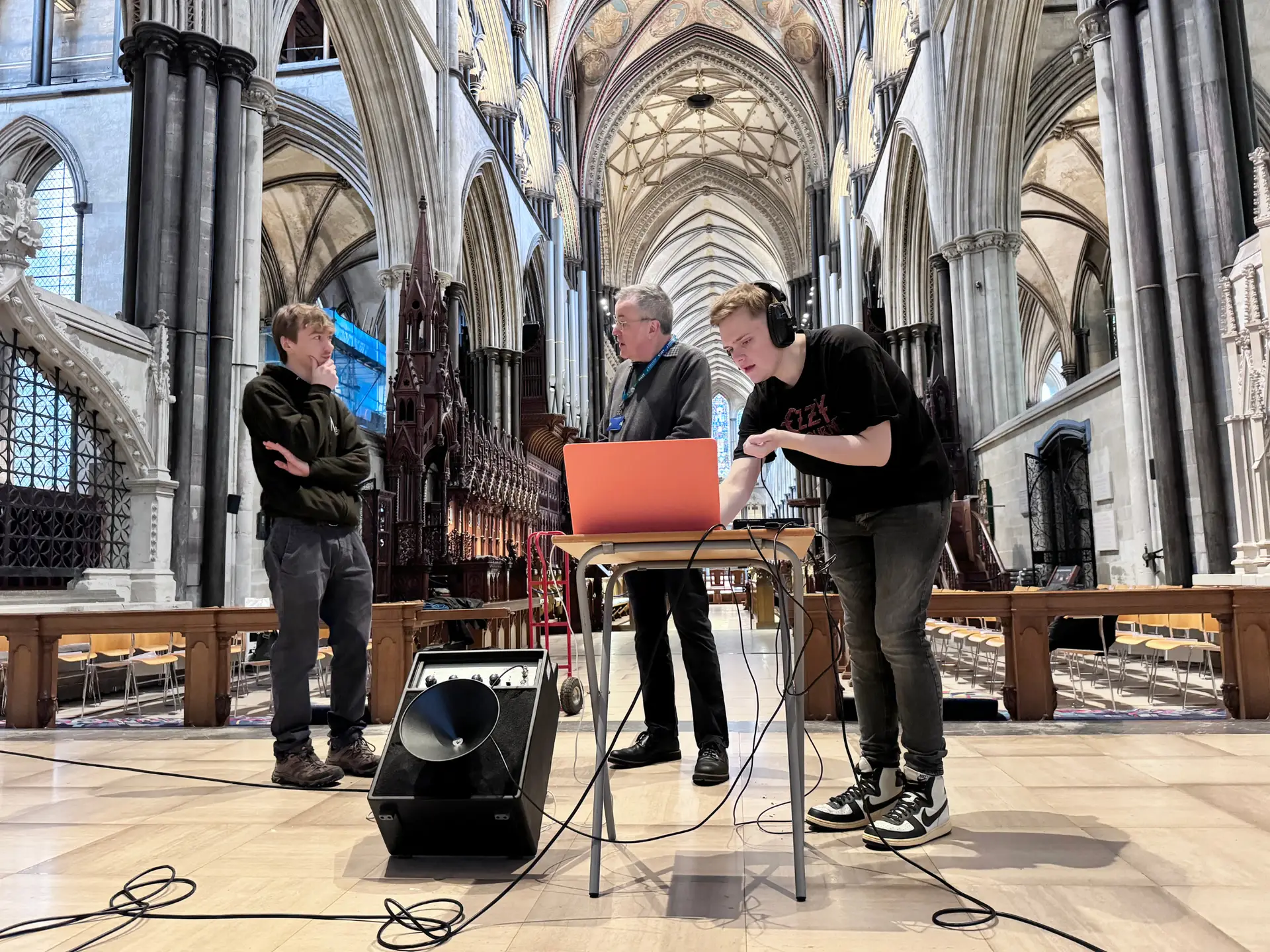 Music students and a lecturer set up recording equipment and a laptop inside Salisbury Cathedral, capturing the building’s acoustics using a speaker and microphones.