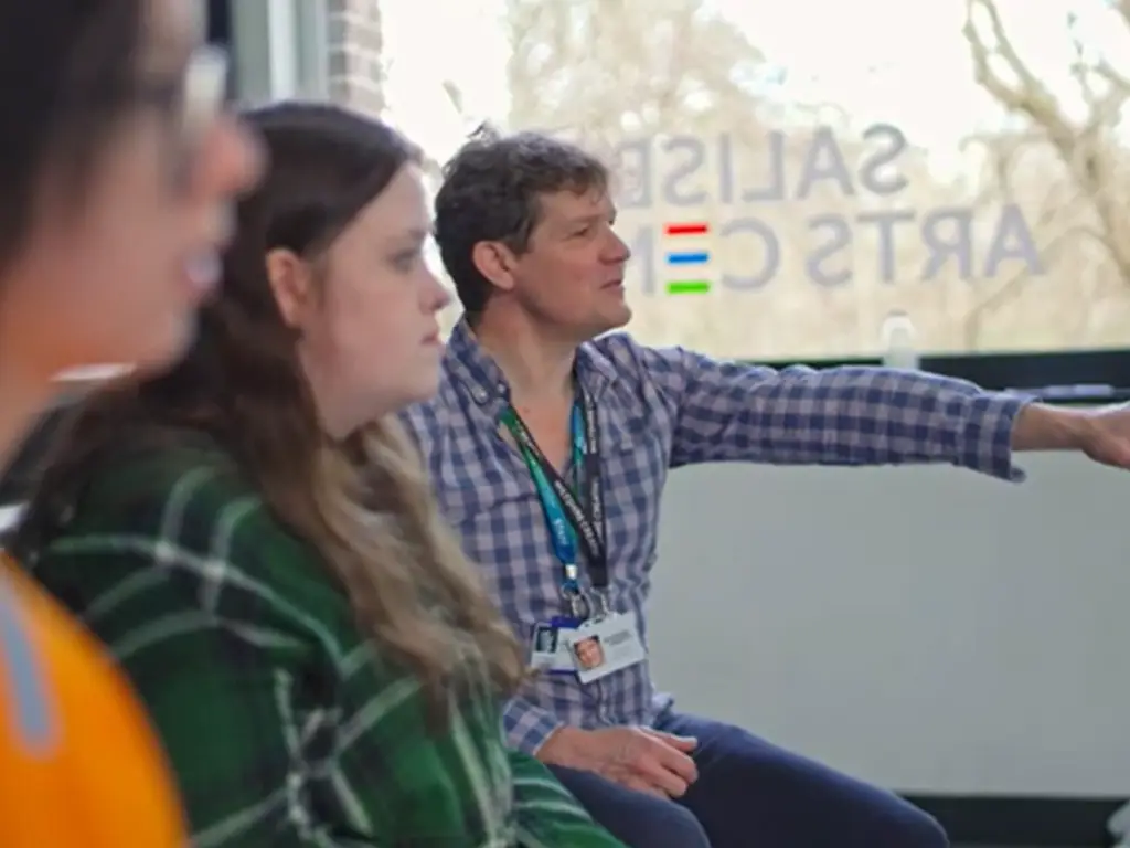 Lecturer sat next to two students. Teacher is guiding someone out of shot