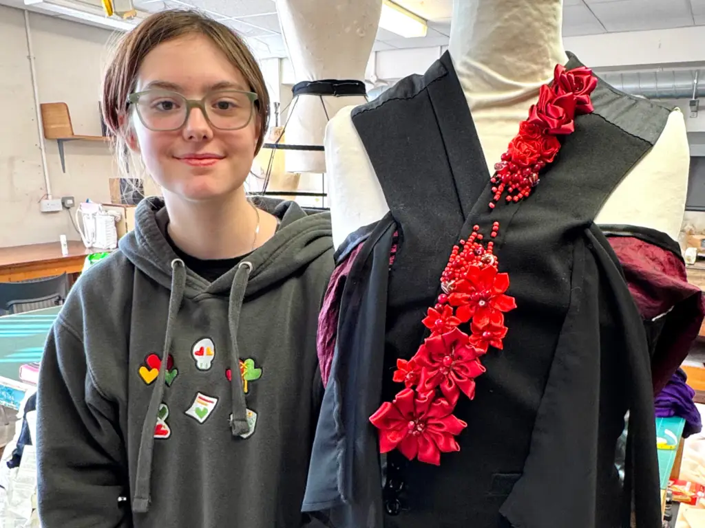 Fashion student stood next to a mannequin displaying her wrap-around top creation