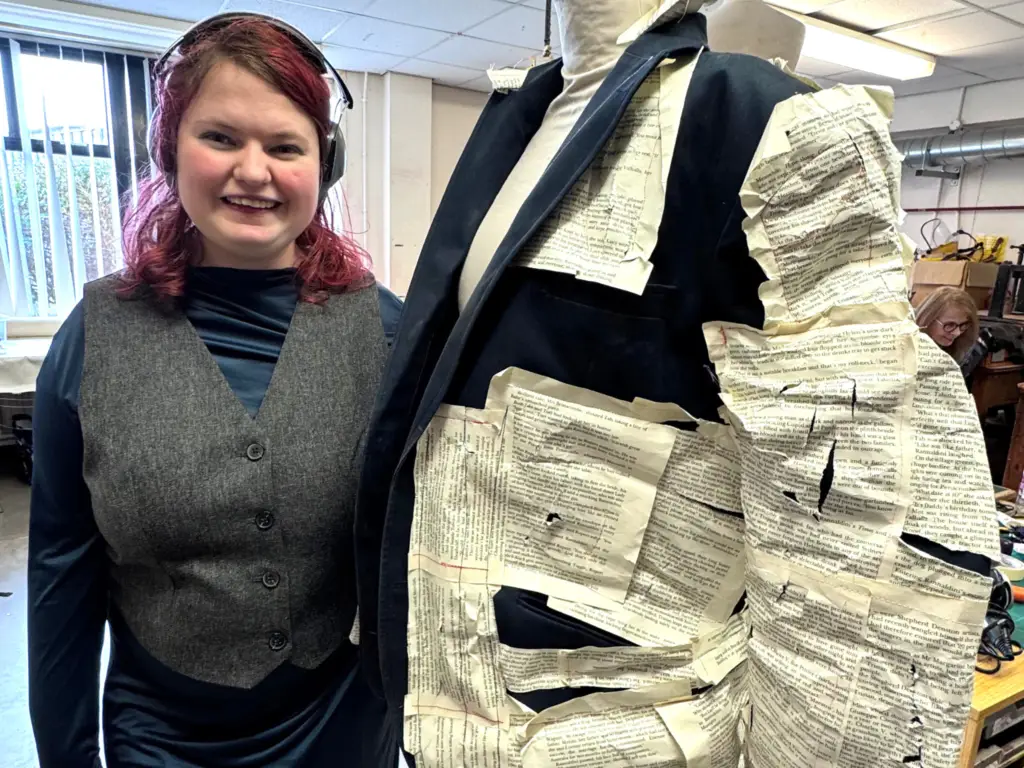 Fashion student stood next to her design of a jackets with pages from a book.