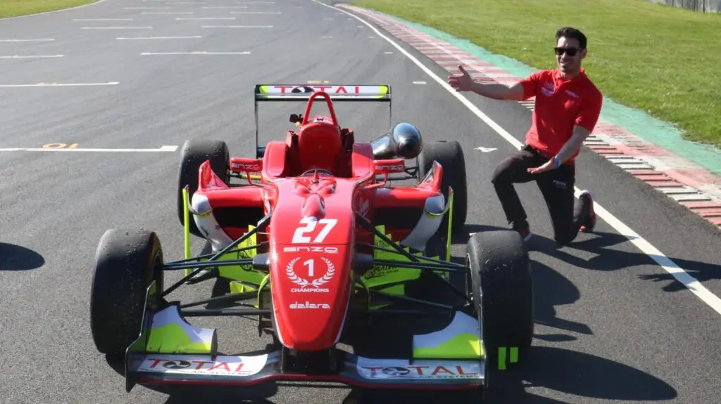 Red racing car on track with a man knelt by it with his thumb up