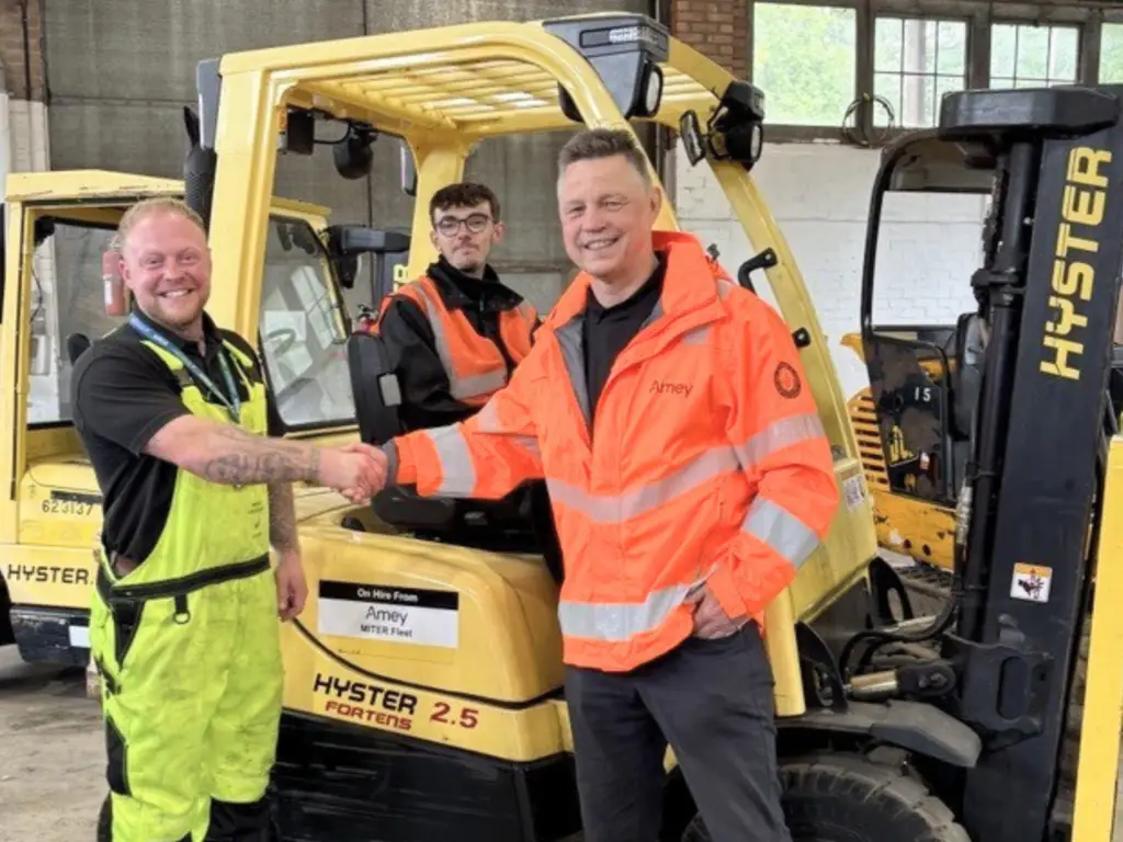 Amey representative shaking hands with a lecturer from Wiltshire College & University Centre with a student in the background on a forklift