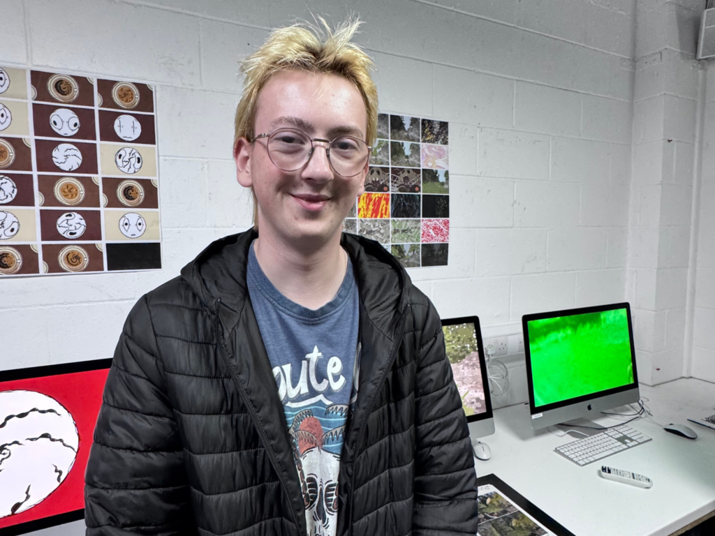 Student standing beside a display of creative work and digital screens during the Trowbridge end-of-term exhibition.