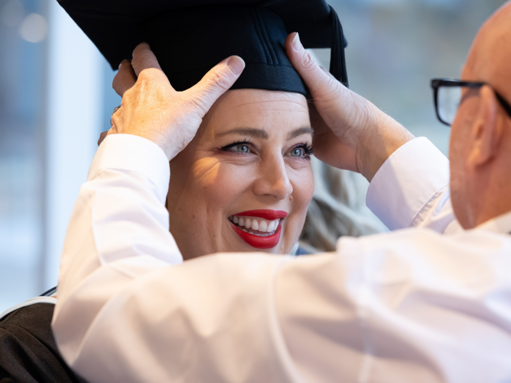 A female graduant smiles as she has her cap fitted 