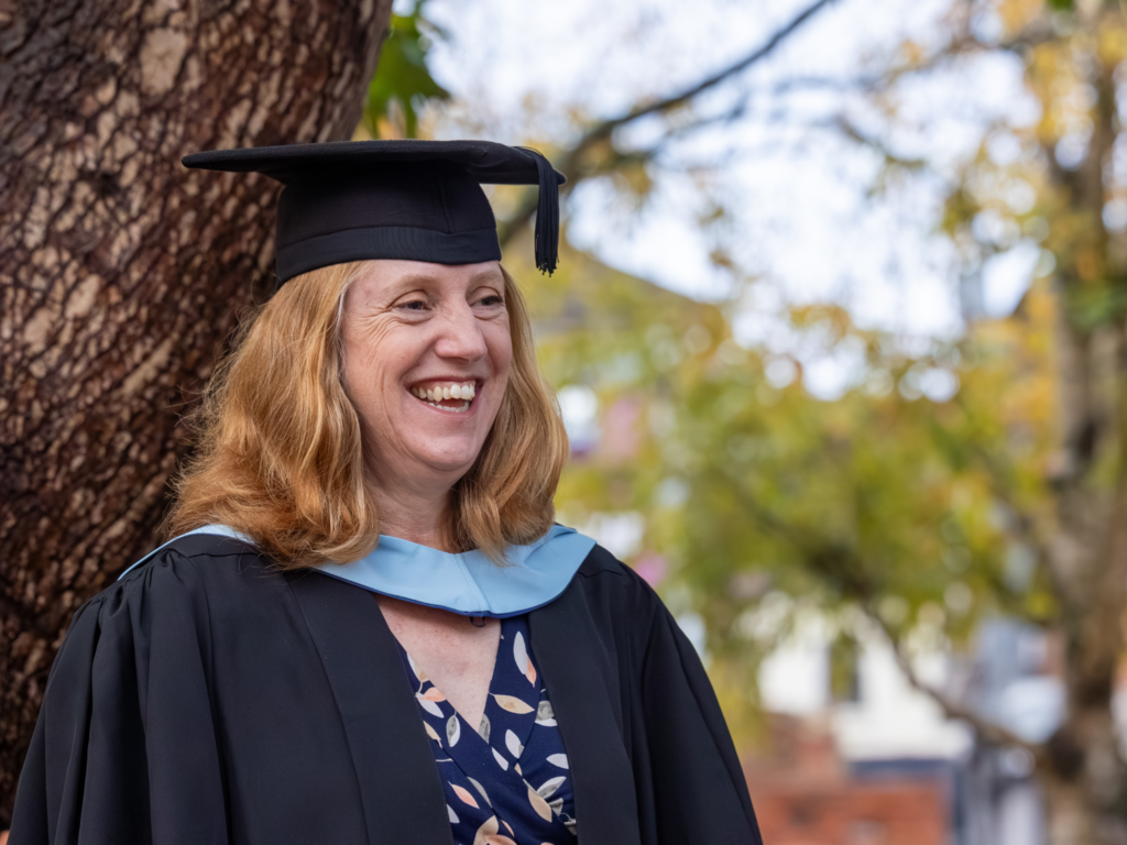 A mature graduand stood by a tree smiling 