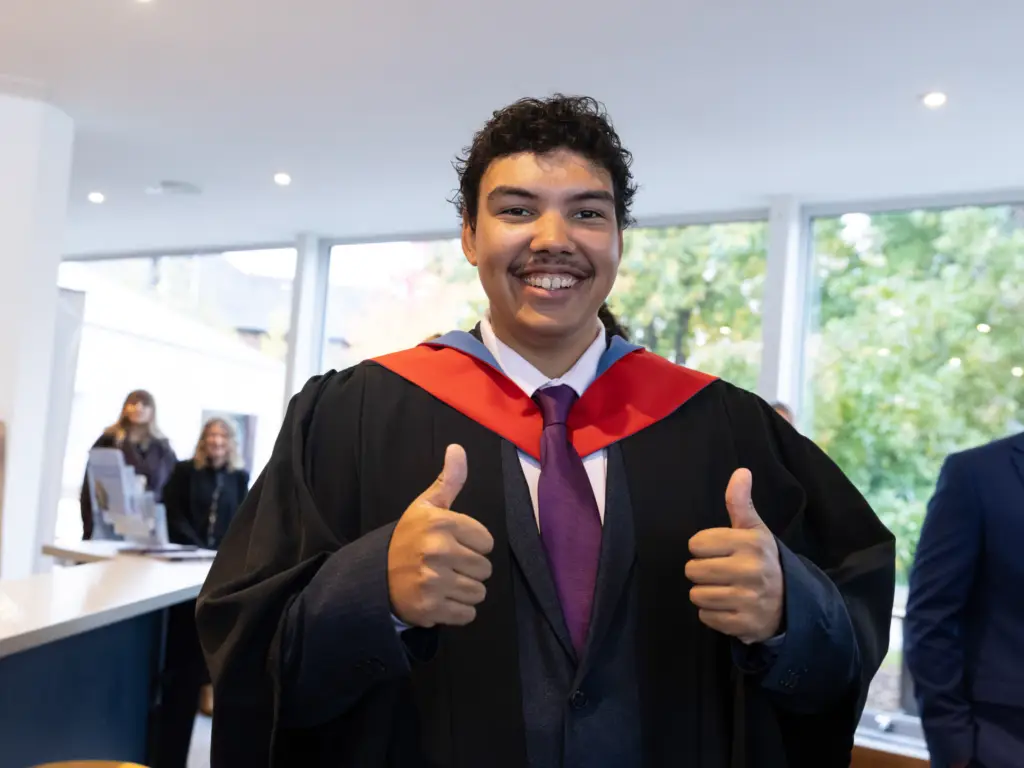 A graduand doing a thumbs up as he waits for his cap 