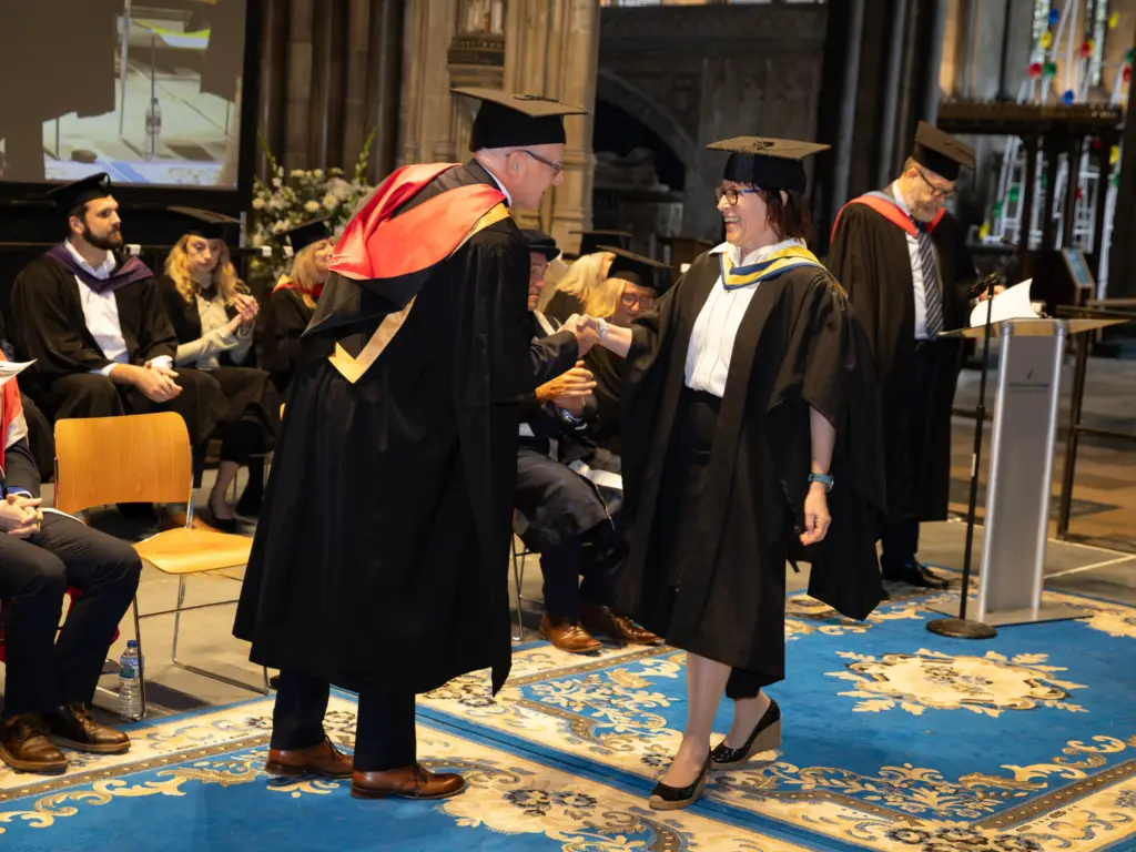 A graduate shaking hands with Paddy Bradley MBE on the graduation stage.